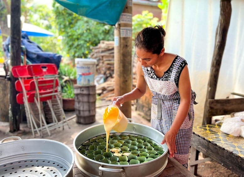 A person pouring yellow liquid into a large metal container filled with green objects. 5