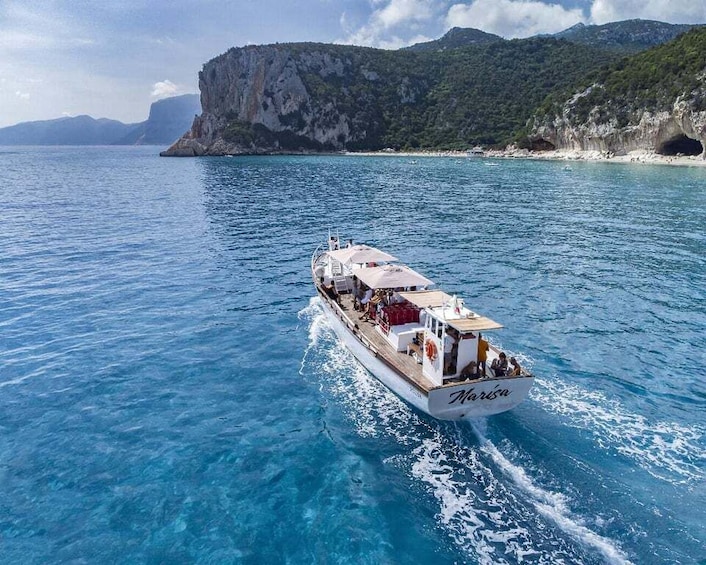 A boat named "Marisa" on a clear blue sea with a rocky coastline and a mountain in the background. 5