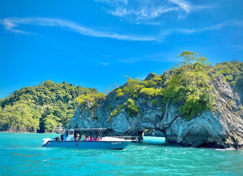 A boat with passengers near a rocky island surrounded by clear blue water. 5