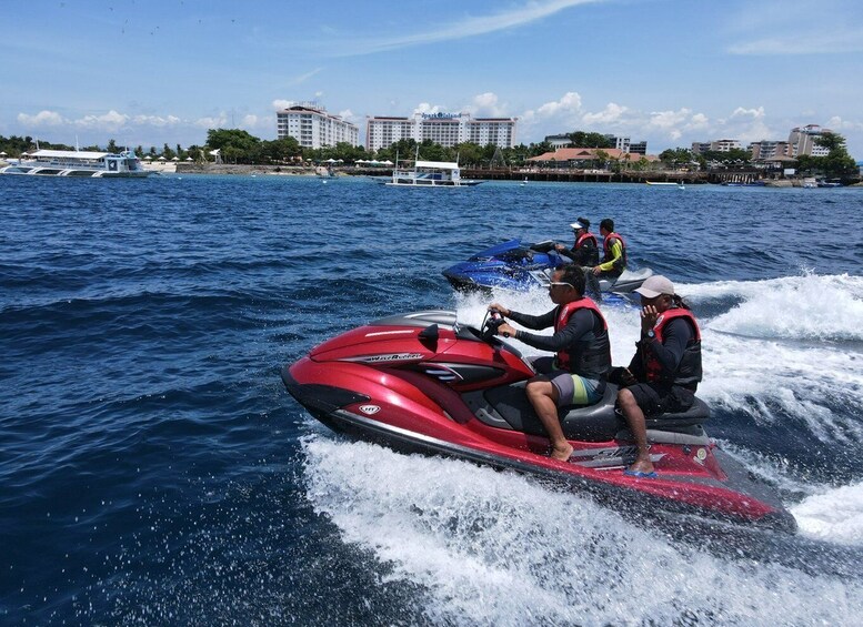 A red jet ski with two riders and a third person in the background. 1