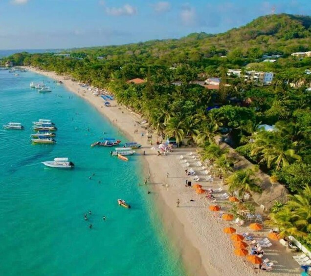 A beach with clear turquoise waters, boats, and palm trees. 5