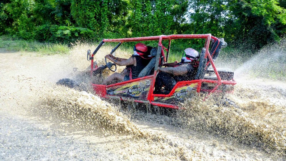 A person driving a red off-road vehicle through a muddy area, splashing mud. 4