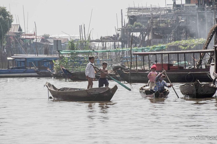 People in small boats on a calm waterway, surrounded by makeshift structures and other boats. 3