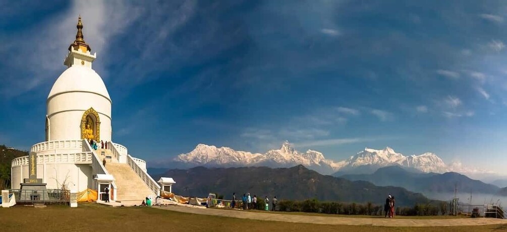 A white stupa with a golden statue, surrounded by a grassy area and a mountain range in the background. 1