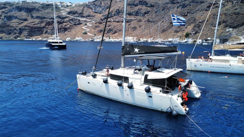 Una barca a vela con una bandiera greca, ancorata in un porto con colline rocciose sullo sfondo. 2