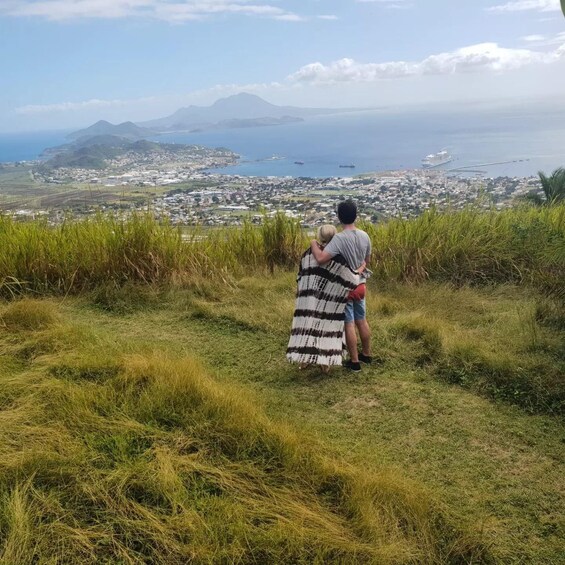 A couple embracing on a grassy hill overlooking a coastal cityscape with ships in the harbor. 4