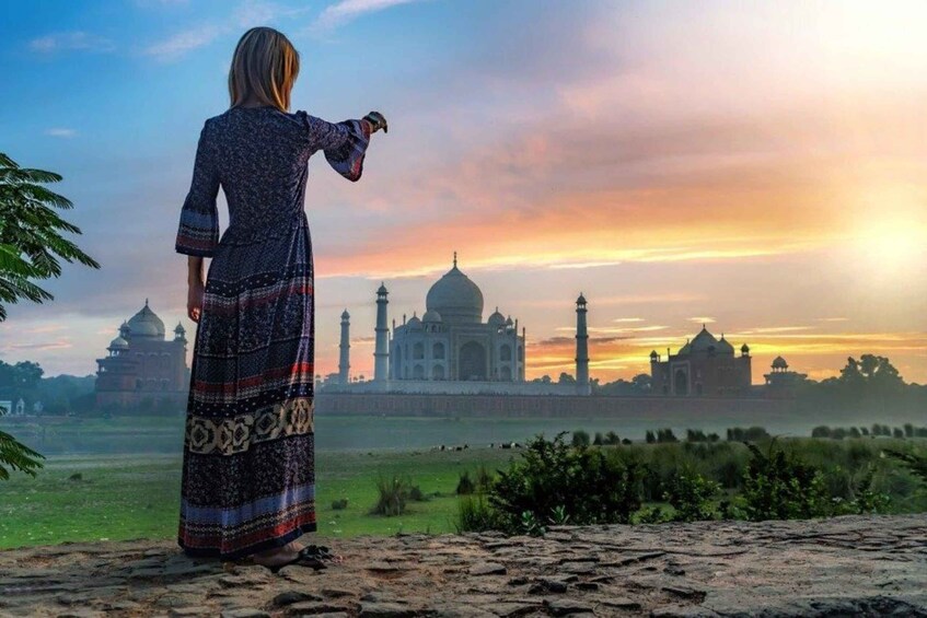 Une personne portant une robe à motifs, debout sur une plateforme en pierre, contemple le Taj Mahal au coucher du soleil. 3