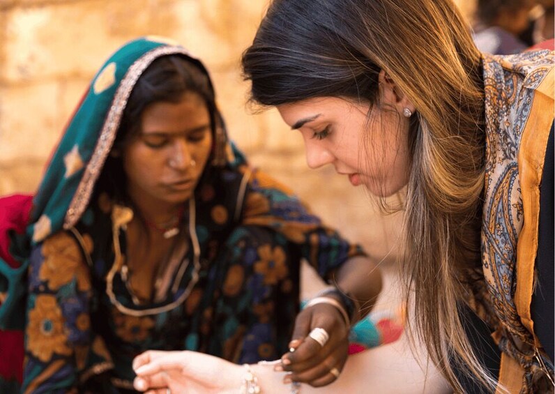 Two women in traditional attire, one applying a bracelet to the other's wrist. 5