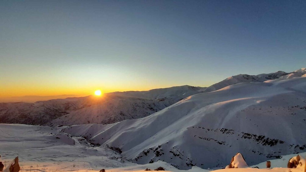 Lumipeitteinen vuoristo auringonnousun aikaan, aurinko matalalla horisontissa. 4
