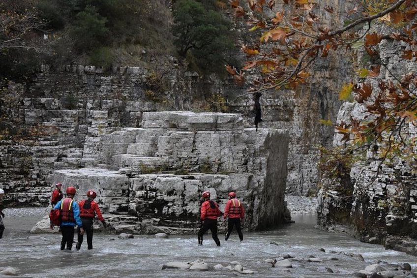 Un grupo de personas con chaquetas rojas caminando por un sendero pedregoso rodeado de muros de piedra y hojas otoñales. 3