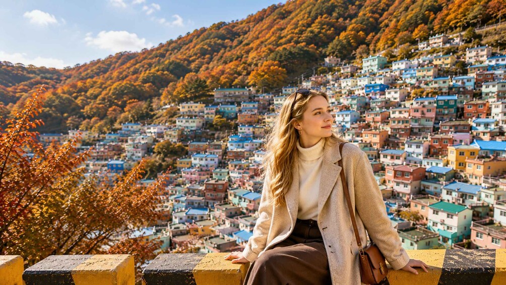 A person sitting on a ledge overlooking a colorful hillside town with autumn foliage. 1
