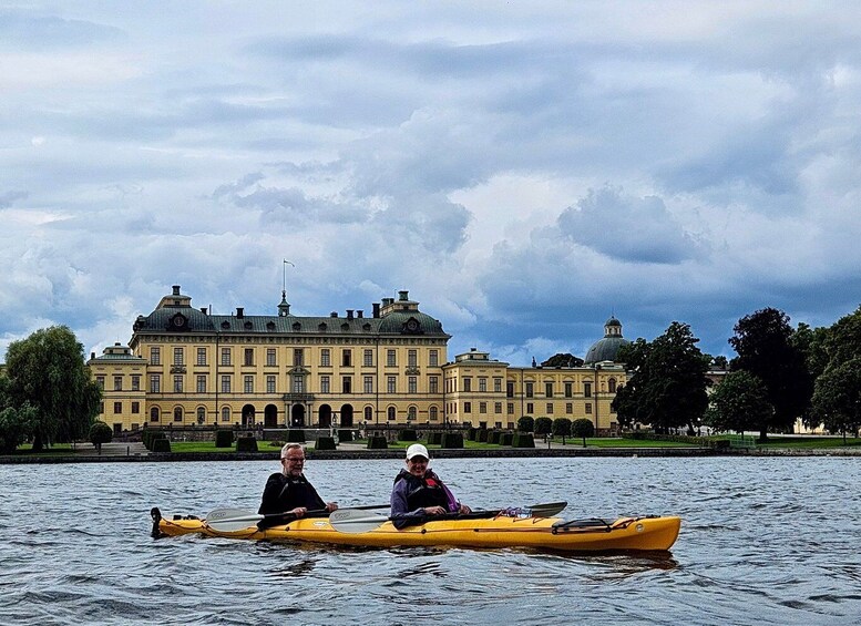 Two people kayaking on a calm lake with a historic building in the background. 4