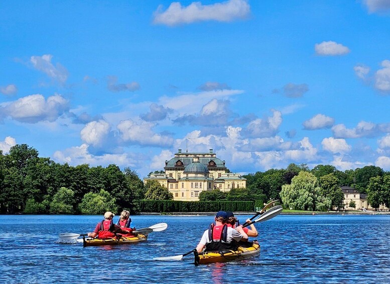 Three kayakers on a lake with a large building in the background. 1