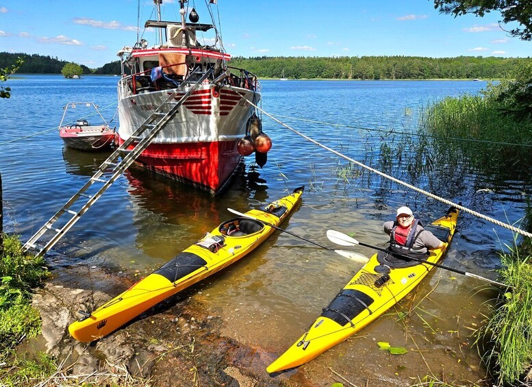 Two yellow kayaks on a rocky shore with a red and white boat in the background. 3