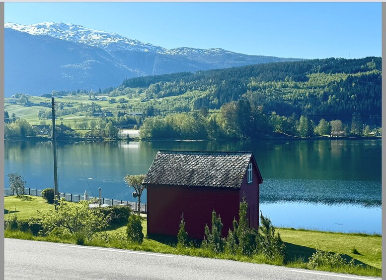 A lake with a red house in the foreground, surrounded by green hills and snow-capped mountains in the background. 2