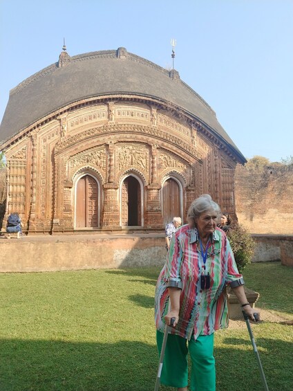 An elderly person with a walking stick in front of a large, intricately carved building with domes and arched doorways. 5