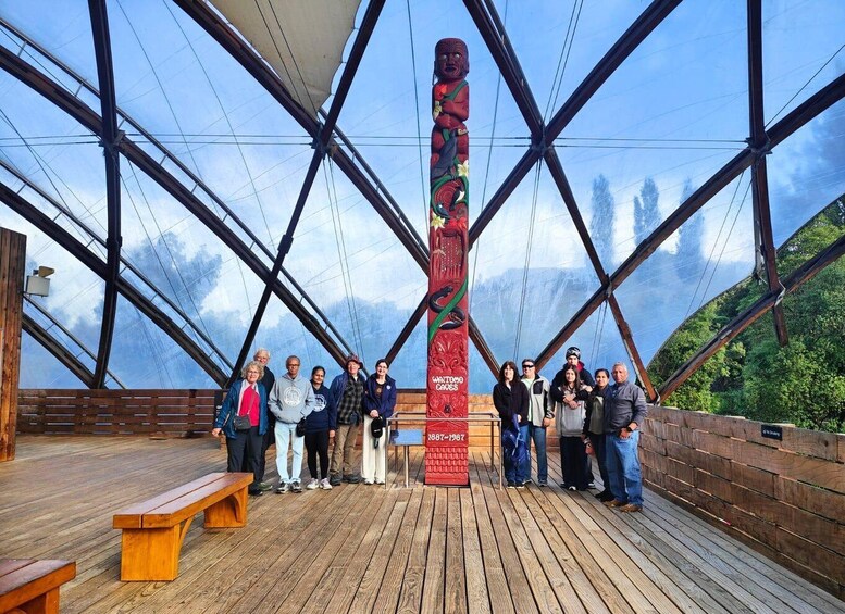A group of people standing on a wooden deck with a totem pole in the center. 2
