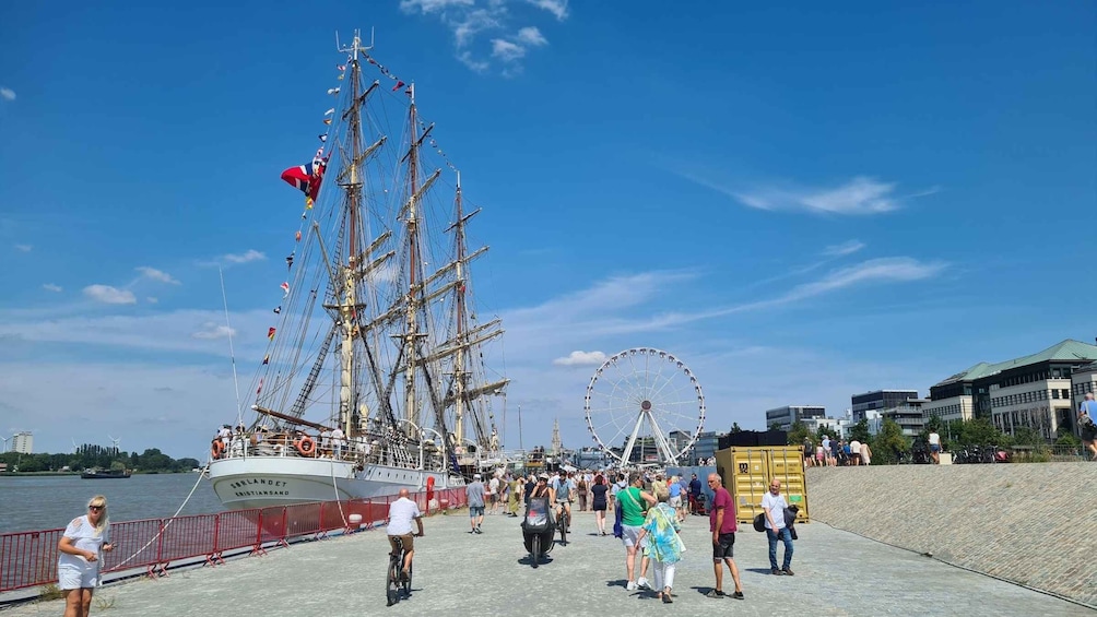 A tall ship with flags, a Ferris wheel, and people on a boardwalk. 1