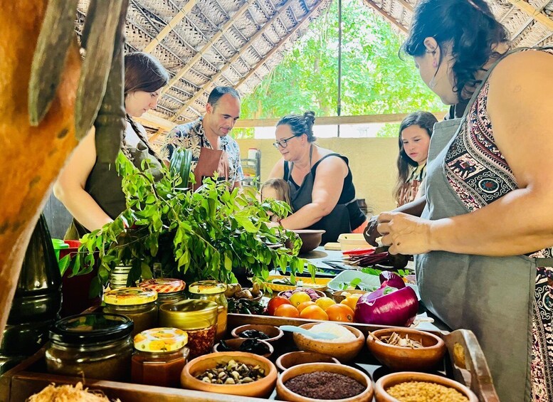 A group of people preparing food in a rustic setting with various ingredients and spices displayed. 1
