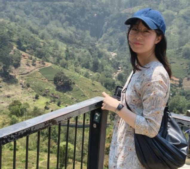 A person standing on a railing overlooking a valley with terraced fields. 4