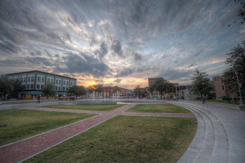 A park with a fountain, pathways, and buildings in the background during sunset. 3
