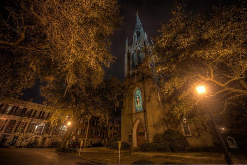 A historic church with a tall spire and stained glass window, surrounded by trees and illuminated by street lamps. 4