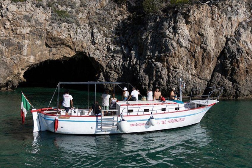 A boat with people on it near a rocky coastline with a cave entrance. 3