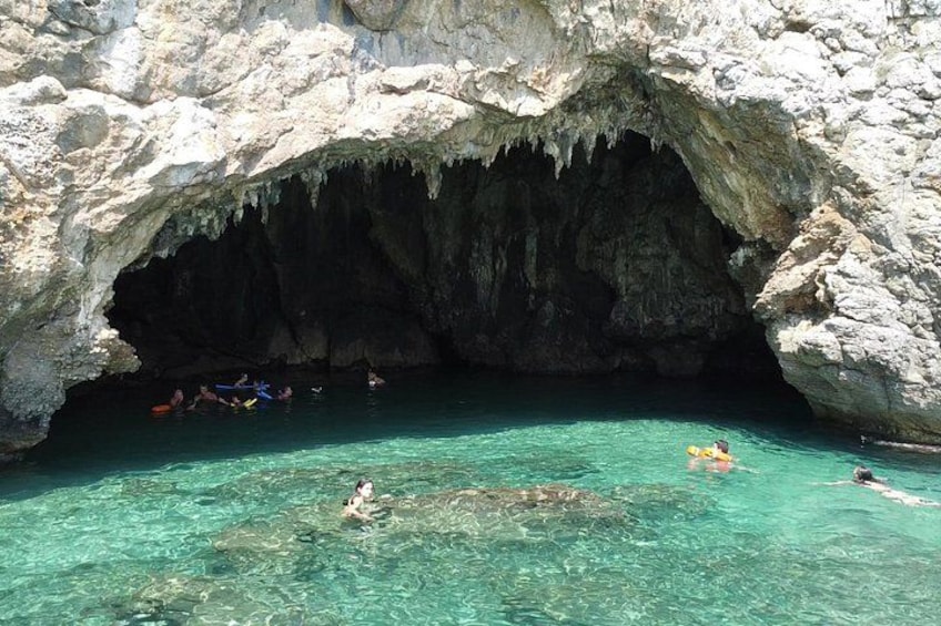 A cave entrance with clear turquoise water and people swimming. 5