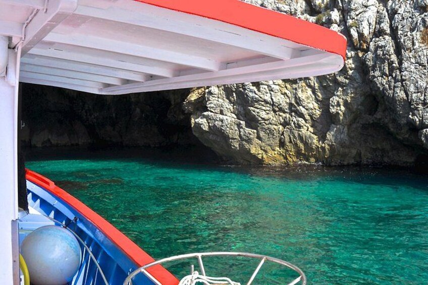 A boat with a red canopy, clear turquoise water, and rocky cliffs. 1