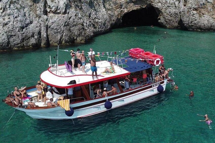 A boat with people on it, a rocky cave in the background, and clear water. 4