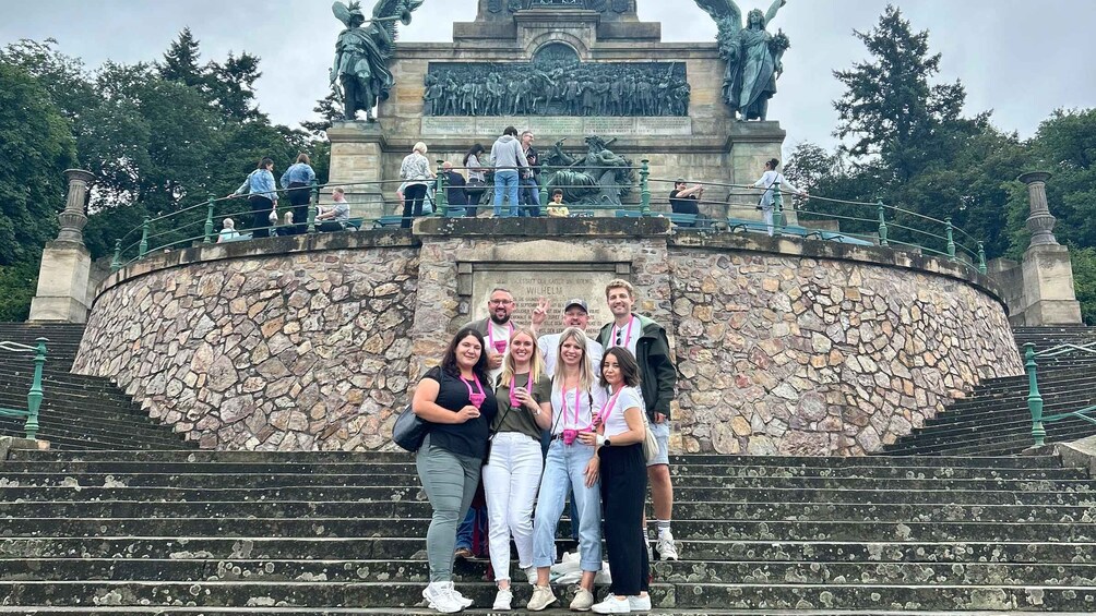 A group of people posing in front of a historical monument with a statue and inscriptions. 2