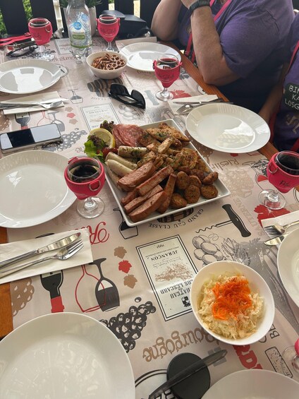 A table set with plates, glasses, and a variety of food including sausages, a salad, and a bowl of coleslaw. 4