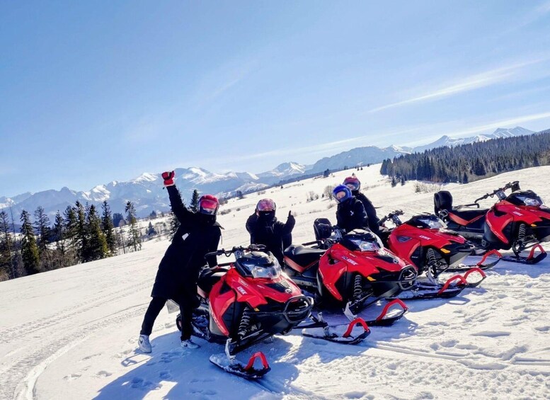 A group of people on snowmobiles on a snowy mountain with a clear sky. 1