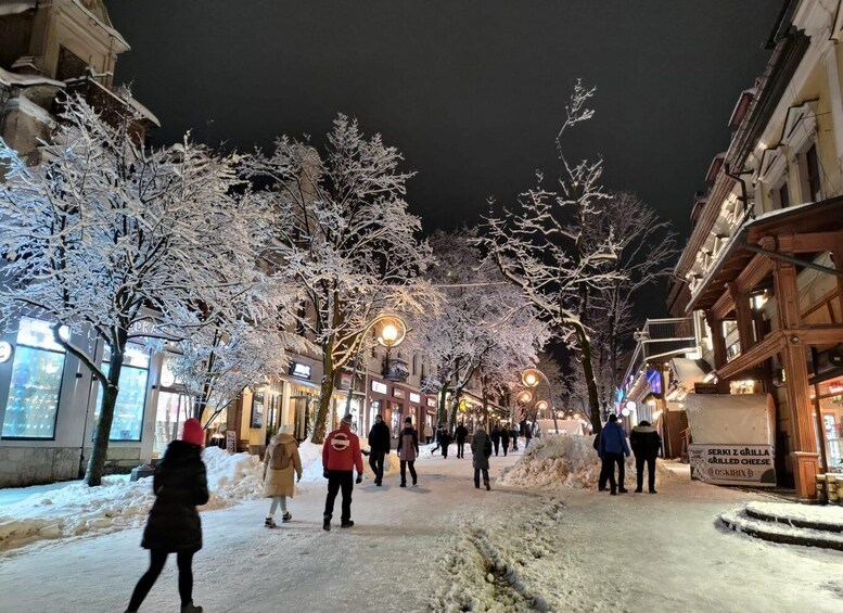 A snow-covered street at night with people walking, illuminated buildings, and a sign for a grilled cheese restaurant. 2