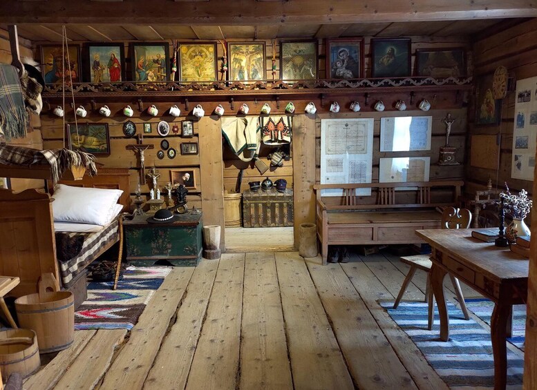 A rustic wooden room with a wooden floor, a bench, a table, and various framed pictures and decorations on the walls. 4