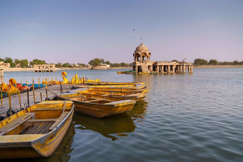 A calm river with several boats docked, a small pavilion, and distant buildings. 5