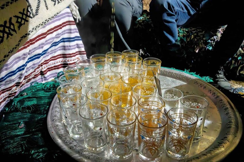 A tray of glasses filled with a yellowish liquid, possibly tea, on a patterned cloth. 4