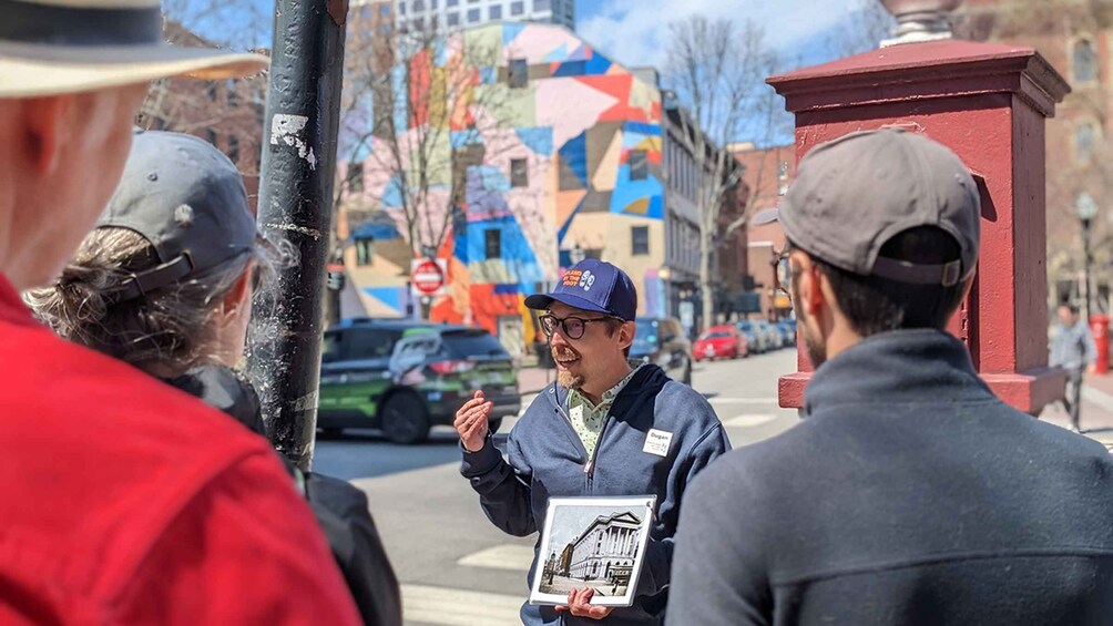 A person holding a book and gesturing to a group of people on a city street. 2