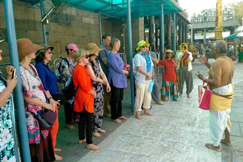 A group of people standing in line, some wearing traditional attire, in an outdoor setting with stone columns and a covered walkway. 1