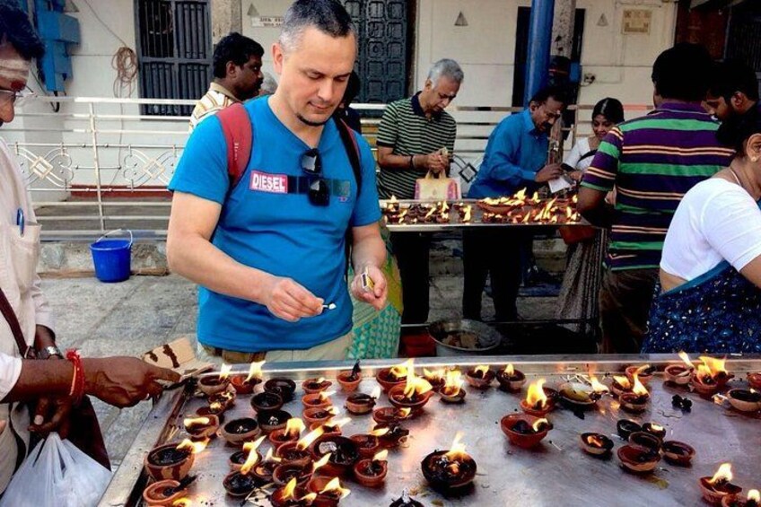 A man in a blue shirt with a camera around his neck, standing at a table with lit oil lamps. 2