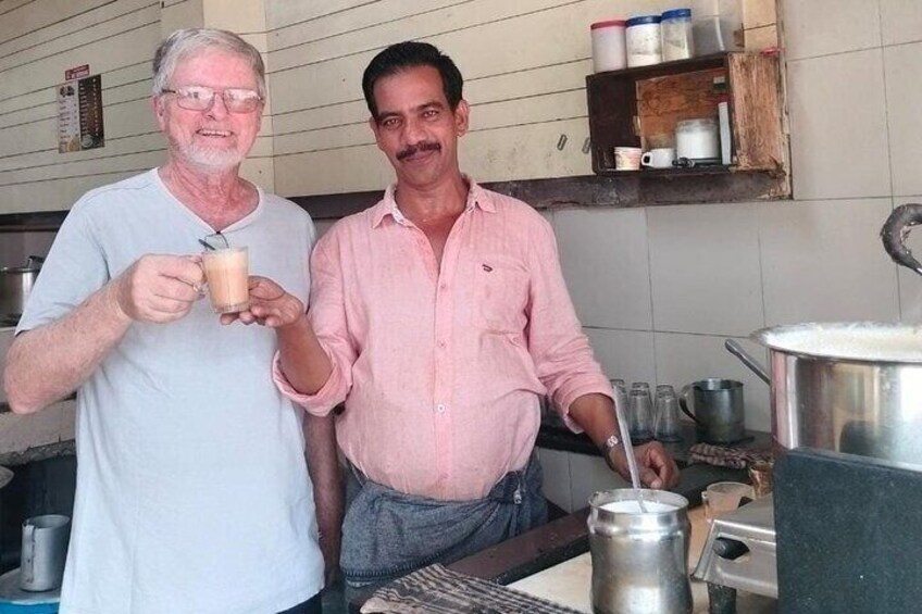 Zwei Männer in einer Küche, einer hält eine Tasse, und verschiedene Küchenutensilien wie ein Topf und Behälter stehen auf Regalen. 5