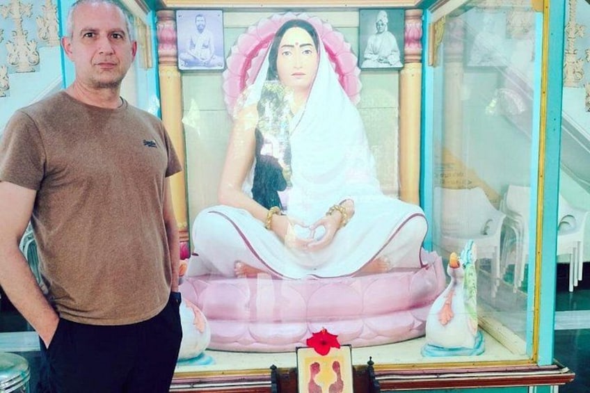 Ein Mann steht neben einer Statue einer sitzenden Figur in traditioneller Pose, mit einem Kissen und einer kleinen Statue daneben. 3