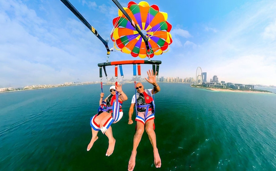 Two people parasailing over a body of water with a city skyline in the background. 2