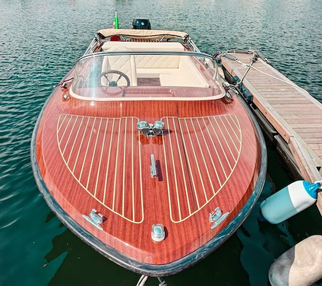 A wooden boat docked at a pier with a clear canopy, a steering wheel, and a green flag. 1