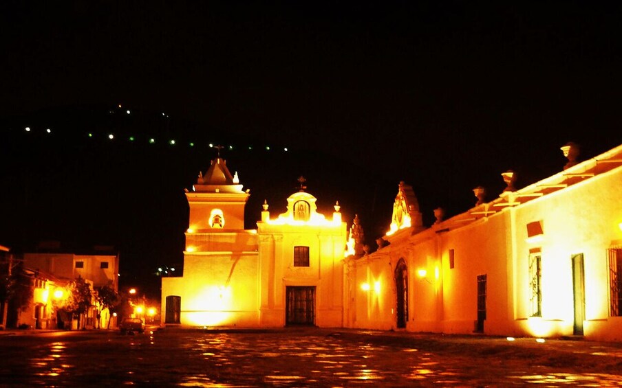 A brightly lit church with a bell tower and a courtyard at night. 3