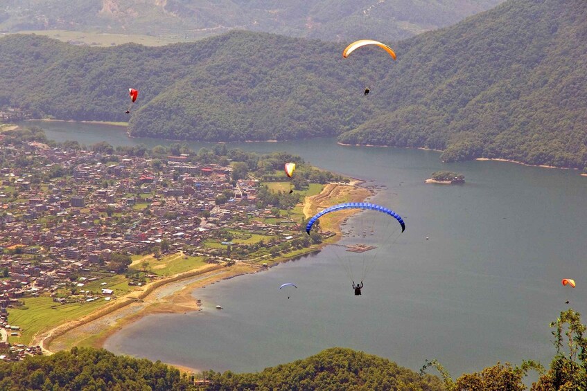 A lake surrounded by hills with several paragliders in the air. 2