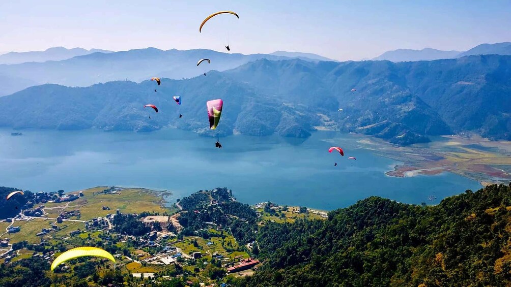 Paragliders flying over a lake surrounded by mountains. 3