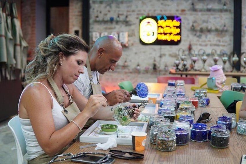 Deux personnes sont assises à une table devant divers pots contenant des produits colorés, probablement destinés à la vente ou à l’exposition. 5