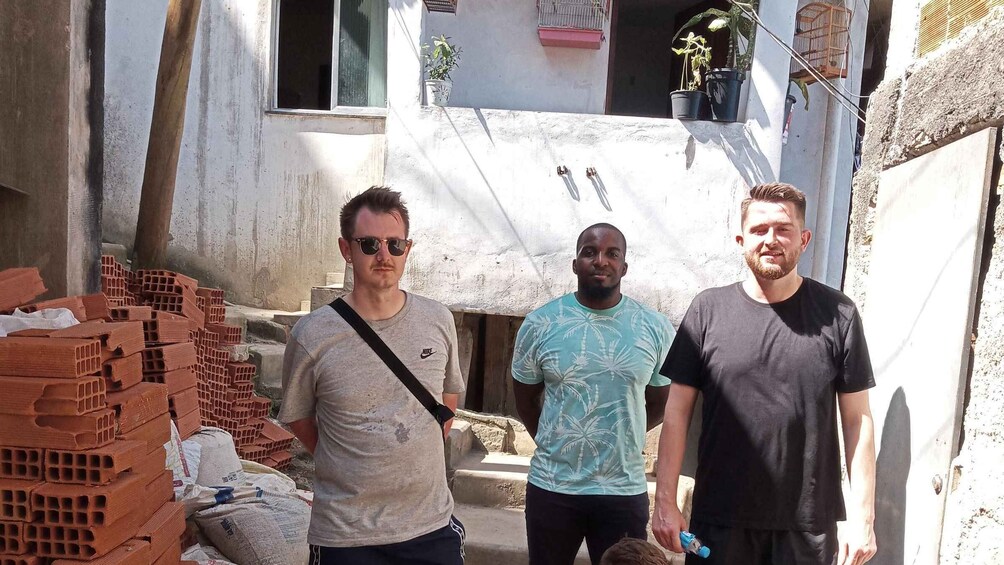 Three men standing in a construction site with brick walls and potted plants. 2