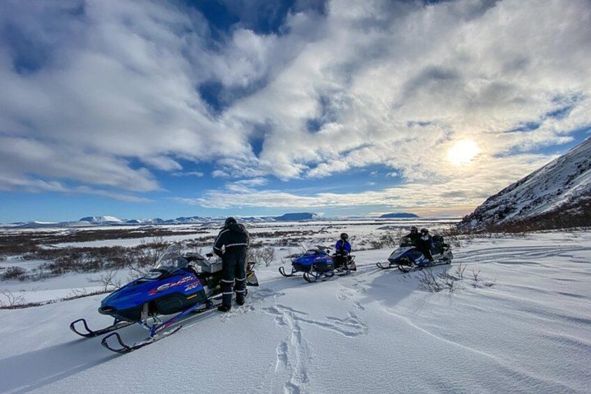 A snowy landscape with three snowmobiles and a person standing on the snow. 3